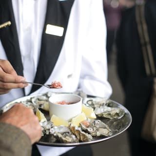 A hand spooning caviar onto ice-chilled oysters with lemon wedges on a silver tray