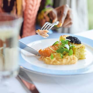A diner tucks into a dish of salmon and potato, garnished with a generous portion of caviar and peppery watercress