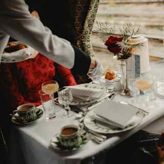 A waiter places a pastry on the plate of a woman in red at a table for two, with coffee cups and glasses of pink Champagne.