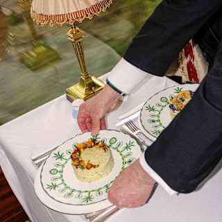 Angled image of a dining table as a waiter sets down a plate of Goat's Cheese Mousse with Fennel Remoulade and beet garnish.