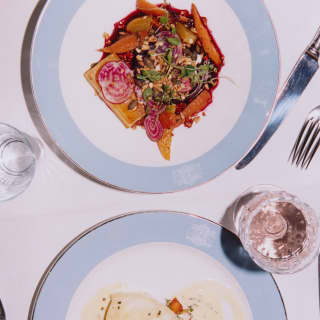 Looking down on plates of Heirloom Carrot Mille-feuille and white fish in a cream sauce, served on blue and white fine china.