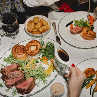 Diners enjoy roast beef, presented in slices with Yorkshire puddings, carrots, beans, potatoes and gravy, seen from above.