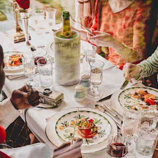 Four guests enjoy a vibrant lunch at a table busy with glasses of red wine, water and Champagne, seen from above, close-up.