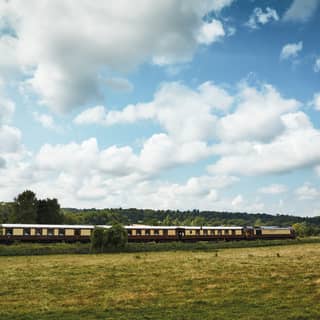 Below a huge sky peppered with cumulonimbus, the cream and burgundy British Pullman glides elegantly between hawthorn
