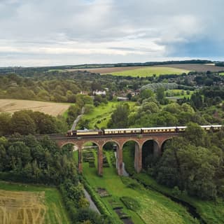 A birdseye view of the British Pullman crossing the arches of the Eynsford Viaduct, with glimpses of the village in the distance