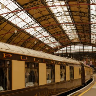 View along the maroon and cream exterior of the British Pullman, stabled beneath the iconic roof of Victoria Train Station.