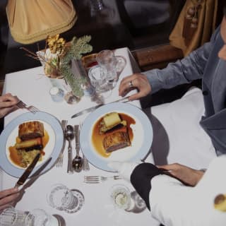 A waiter serves food to a festive table where two guests prepare to feast on sensational Beef Wellington, seen from above.