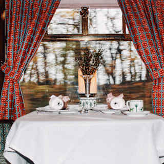 Eye-level view of a Cygnus Car dining table with teacups and Christmas crackers, framed by vivid orange and blue curtains.