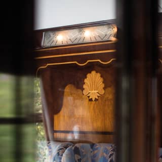 View through a glass partition of a blue-patterned armchair under ornate marquetry