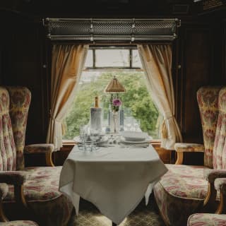 View from one table across the aisle to another laid for dinner with Champagne in a cooler, illuminated by soft window light.