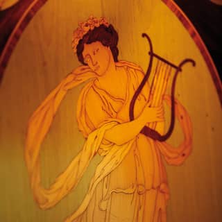 The Greek Muse Erato is depicted in a flowing gown and flower crown playing her lyre in an exquisite example of marquetry
