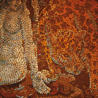 A detailed mosaic in tiny tiles of sunset oranges and reds depicts the Greek goddess, Rhea, holding her open palm to lioness