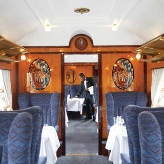 Rows of armchairs and tables either side a vintage train carriage aisle