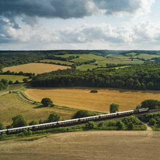 A long train of eight cream and burgundy carriages cuts across the summer fields past harvested fields and a haystack