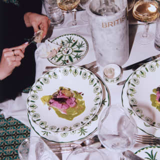 A busy table with crockery from the Sultan's Garden range by William Edwards, vibrant food and wineglasses, seen from above.
