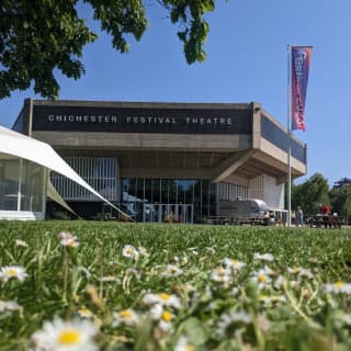 A colourful banner flaps in the breeze outside the Chichester Festival Theatre. A lawn spreads out, dotted with daisies