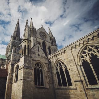 The tall spire of Chichester Cathedral rises high above its green copper roof, gothic arched windows and carved masonry