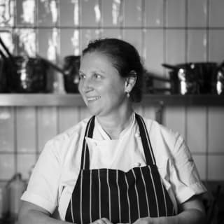 Michelin-starred chef, Angela Hartnett, dressed in chef whites and apron, smiles off camera as she prepares a new potato