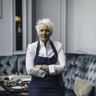 Michelin-starred chef, Lisa Goodwin-Allen, looks at the camera with her arms folded as she leans on a chair in a restaurant