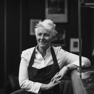 A black and white image of Michelin-starred chef, Lisa Goodwin-Allen, smiling to someone off camera as she leans on a bar