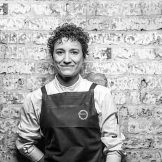 A black and white image of Michelin-starred chef, Nieves Barragán Mohacho, as she leans on a wall in her chef's whites