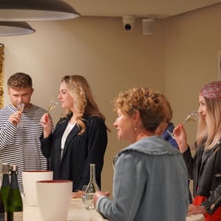 A man in a striped shirt and a woman with blond hair capture the aromas of white wine at a tasting with three other guests.