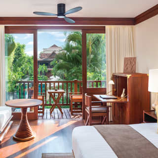 A junior suite with its doors open onto a sunny balcony overlooking the pool and lush tropical gardens