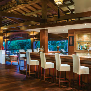 Spacious open-air bar with white leather barstools and polished wooden floors