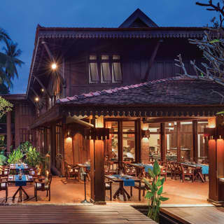 Timber-framed open-air pagoda restaurant terrace dotted with tables and palm plants