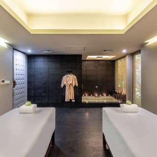 Spacious spa treatment room with two massage tables and a candlelit spa bath