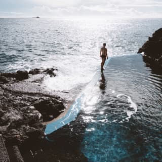 Hombre de pie en el borde de una piscina de agua dulce con vista al océano