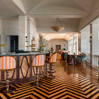 Four orange and white stools circle the bar in the Reid's Palace cocktail room with stunning black and wood chevron parquet.