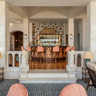 View from the lounge, through salmon-pink chairs, up two stepa to a level with parquet flooring and a stunning cocktail bar.