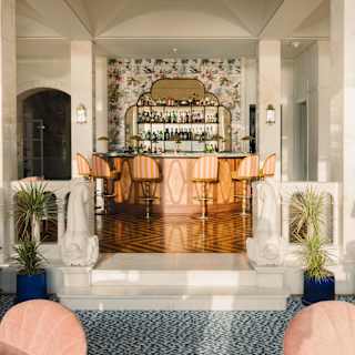 On 1891 Bar's raised parquet floor, six striped stools line a curved counter in front of an Art Deco mirrored bottle shelf.