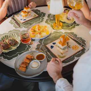 Three friends drink cocktails and enjoy plates such as sliders from 1891 Bar's menu at a table with green floral placemats.