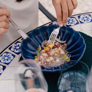 A female diner tucks into a seafood salad served in a blue ceramic bowl, seen from above at a table with wine at Brisa Do Mar.