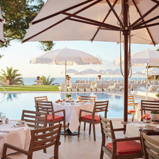 Linen-topped tables under sun umbrellas on a poolside restaurant terrace