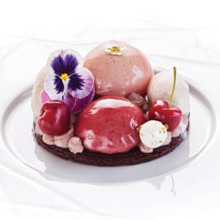 Cherry and vanilla mousse dessert topped with edible flowers and gold leaf