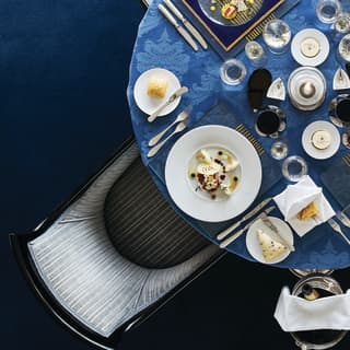Circular table topped with a blue-patterned tablecloth and formal dinner settings