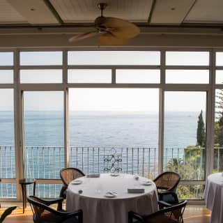 High-angle view featuring two round tables at William Restaurant by a wall of windows, placed to enjoy expansive ocean views.