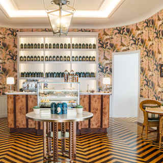 Looking over a chevron-parquet floored room to a bar with backlit shelves of tea canisters and a glass-fronted cake display.