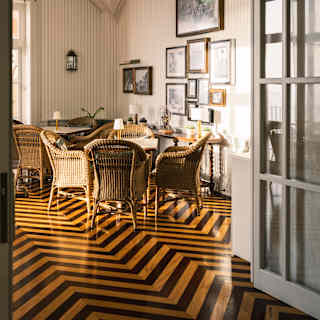 Polished black chevron-stripe parquet leads through a doorway into the bright Tea Library with cane seating and high ceiling.