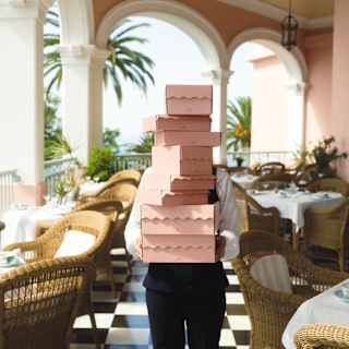 A staff member carries a stack of pink cardboard cakeboxes piled as high as to obscure their face, seen on the Tea Terrace.