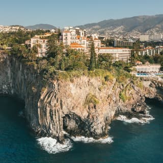 High-angle image of the hotel and gardens, perched on the dramatic, rocky headland, taken from above the aquamarine sea.