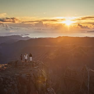 Three guests stand on Madeira's third highest peak, Pico de Arieiro, watching the sun rise over craggy mountains and valleys.