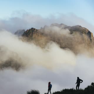 The silhouettes of two hikers on the Levada da Negra stop to view the incredible cloud-shrouded ridge of Pico do Arieiro.