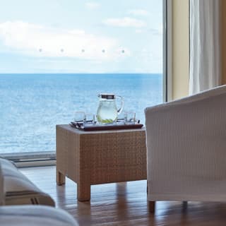 Glass jug of water on a rattan coffee table next to a large window with sea views
