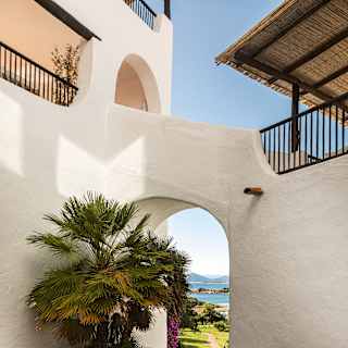 A path flanked by a rockery and a flowerbed with pink and white blooms cuts through an external arch between two residences.