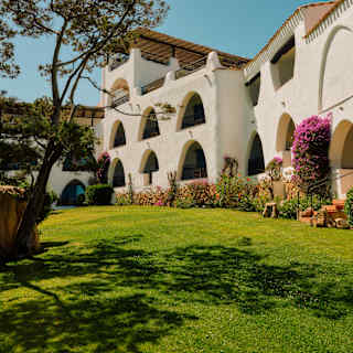 View across green lawn of Romazzino's white rooms with arch and keyhole balcony openings, and roof terraces above.