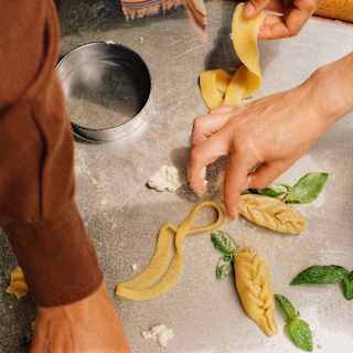 Guests create culurgiones, stuffed pasta with an ear-of-wheat shape, in a cooking class, seen from above, close-up.